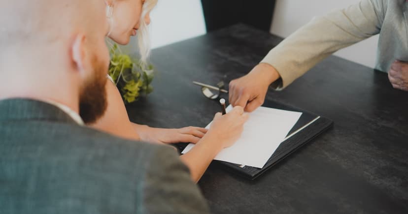 A couple signing a document at a desk while an adviser points to where the signature goes