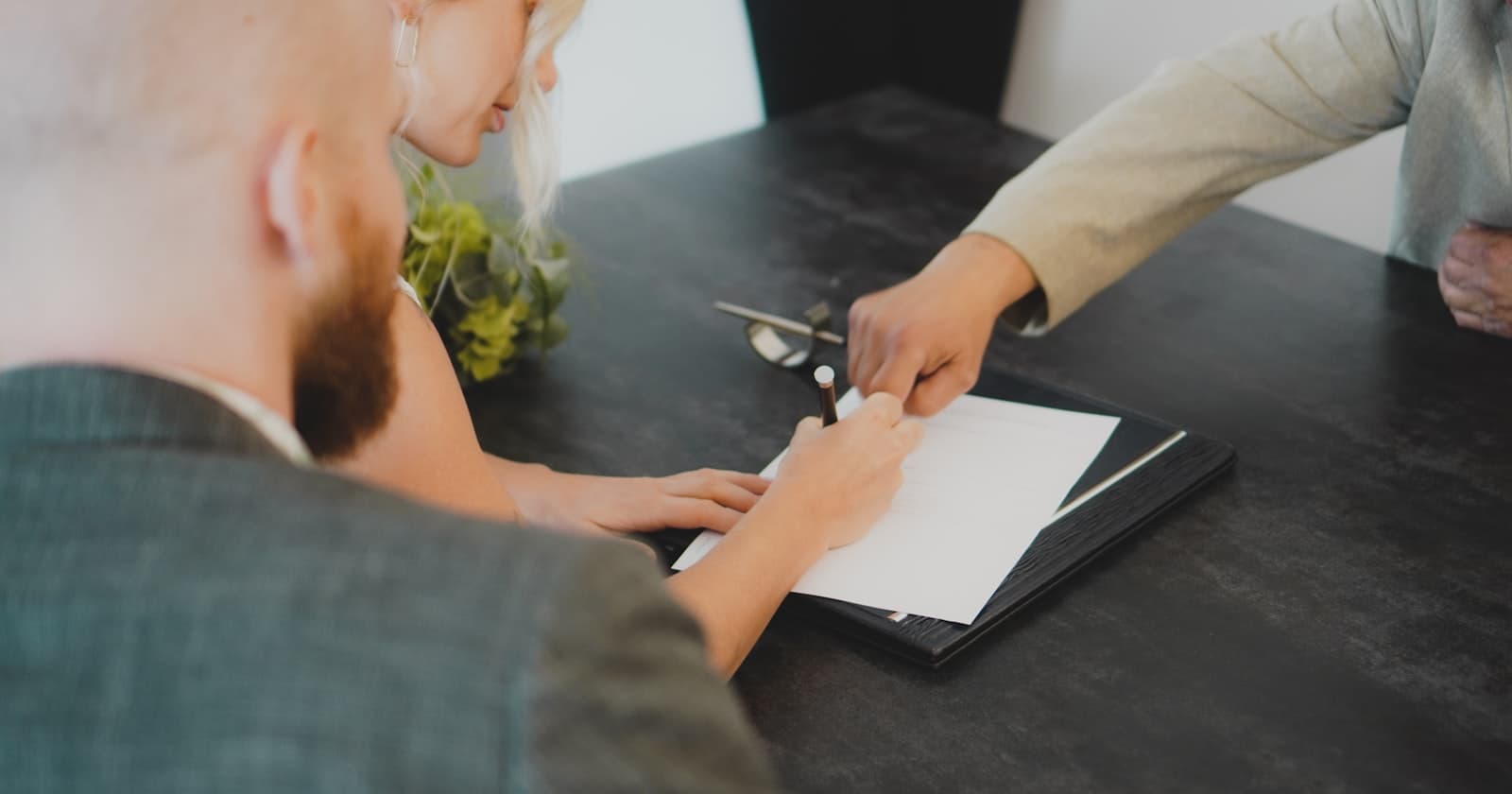 A couple signing a document at a desk while an adviser points to where the signature goes